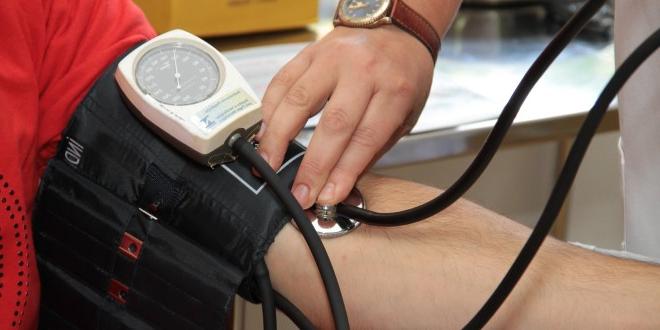 someone taking another person's pulse with a stethoscope and compression sleeve. No people are pictured, just arms and hands. 